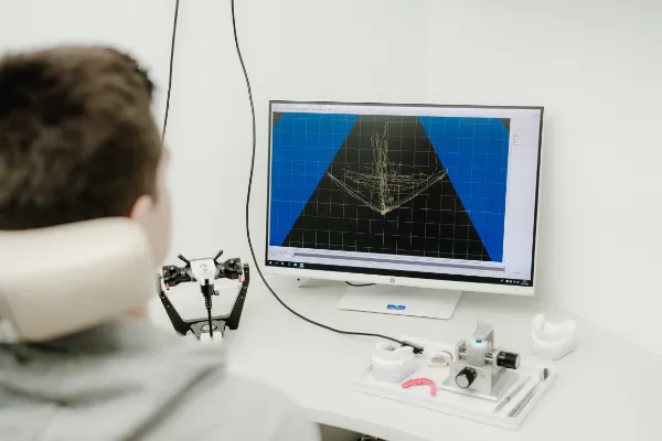 Ein Patient blickt in der Praxis auf einen Monitor, der eine digitale, dreidimensionale Darstellung der Kiefergelenksbewegungen und der instrumentellen Bissanalyse zeigt.
